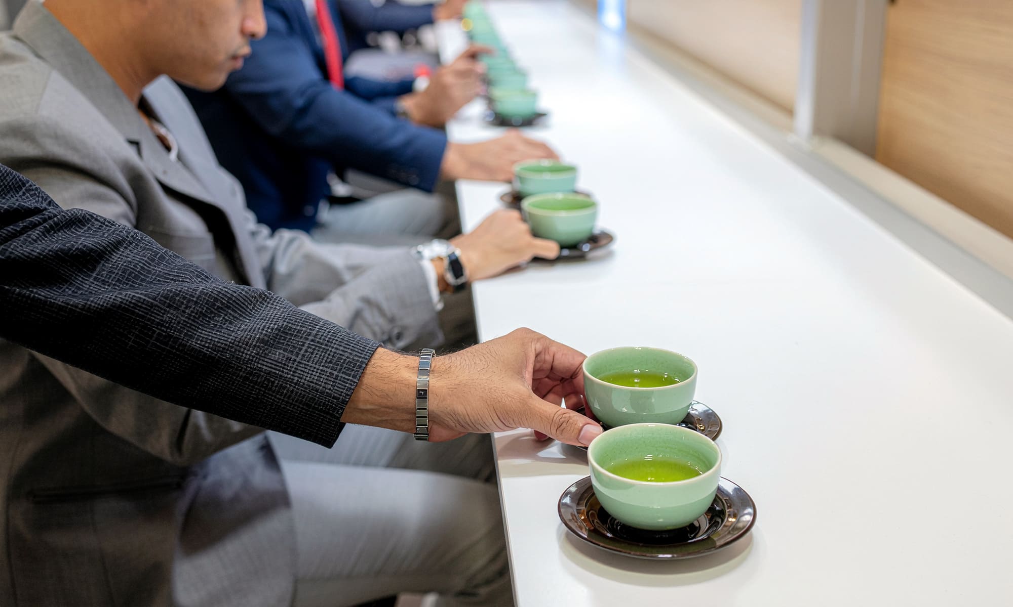 Close-up of tea tasting session with multiple cups of brewed Japanese green tea, professionals evaluating flavor, clean and minimal environment, realistic, B2B setting